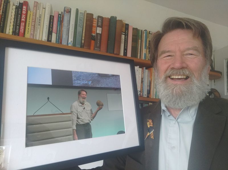 Ian Redmond smiling beside a framed print of himself speaking on stage at Rebalance Earth